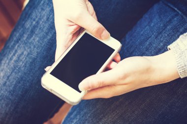 Cep telefonunun yukarıdan aşağı görüntüsü kucağa yakın ve boş ekranlı kot giyen birinin ellerinde.
