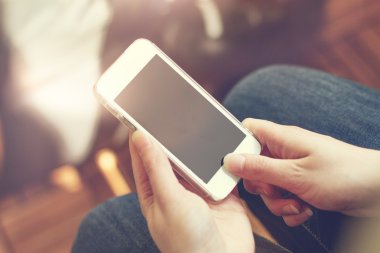 Güneşli odada elinde boş ekranla cep telefonu kullanan kişinin omuz hizasında.