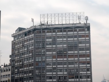 Yana yatık kenarları ve cep telefonu anteni olan modern, yüksek katlı bir apartman.