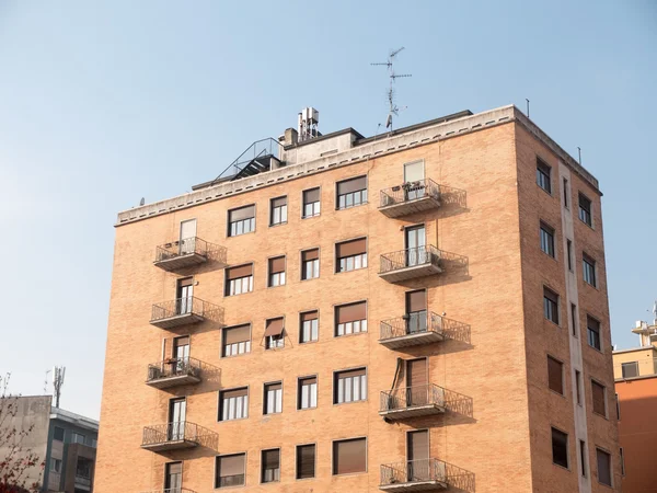 Low Rise Residential Apartment Building with Small Balconies and Brick Facade Illuminated by Bright Sunlight on Sunny Day with Blue Sky