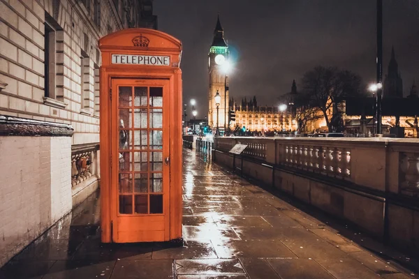 Red British Telephone Booth in London near the Houses of Parliament and Big Ben illuminated on a wet cold night