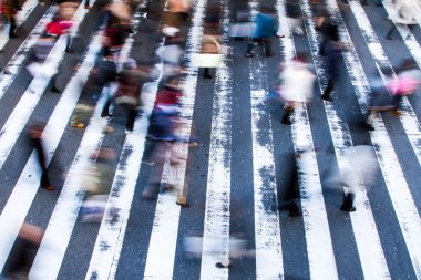 İnsanlar hareket bulanıklığıyla bir zebrayı karşıya geçirip caddelerdeki çizgilere odaklanıyorlar, yüksek açı manzaralı.