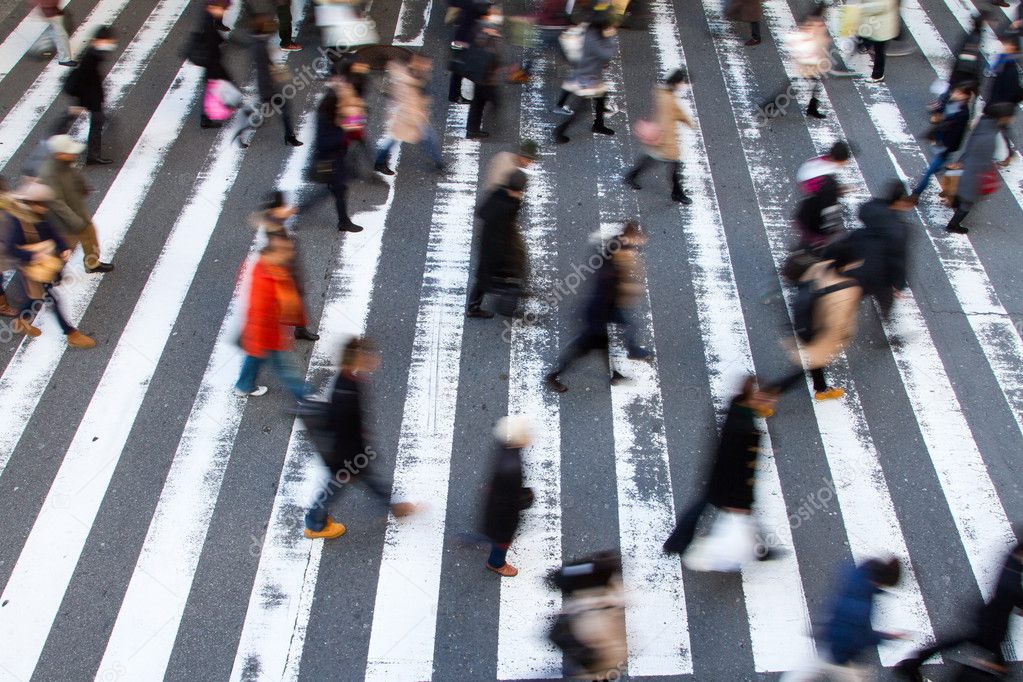 Crowd of pedestrians crossing a zebra crossing in a high angle view with motion blur and focus to the white stripes on the tarmac