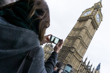 Parlamento binasında, Westminster, Londra 'daki Big Ben Saat Kulesi' nde omuz manzaralı cep telefonuyla fotoğraf çeken bir kadın.