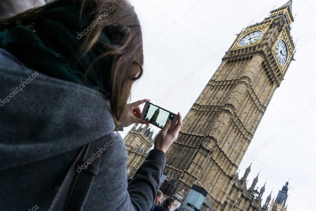Woman tourist photographing Big Ben Clock Tower at the Houses of Parliament, Westminster, London, on a mobile phone, over the shoulder view