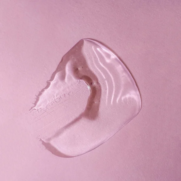Pembe arka planda bir damla şeffaf kozmetik jel.