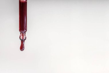 Pipetten bir damla kırmızı serum düşüyor.