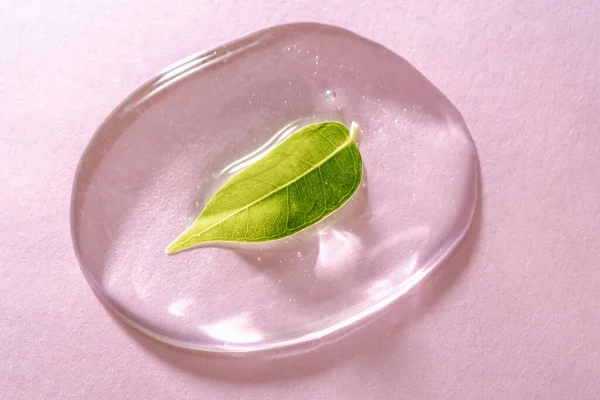 Pembe arka planda bir damla şeffaf kozmetik jel.