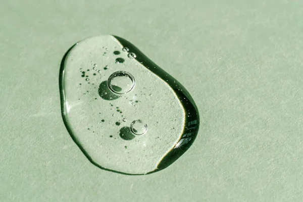 En droppe transparent kosmetisk gel på en grön bakgrund. — Stockfoto