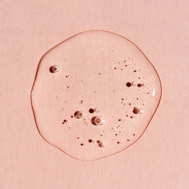 Pembe arka planda bir damla şeffaf kozmetik jel..