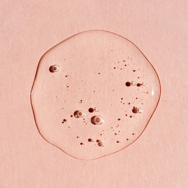 Pembe arka planda bir damla şeffaf kozmetik jel..