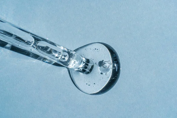 Mavi arka planda bir kozmetik ürünü kabarcıklı bir pipetten çıkar.