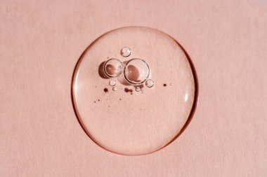 Pembe arka planda bir damla şeffaf kozmetik jel..