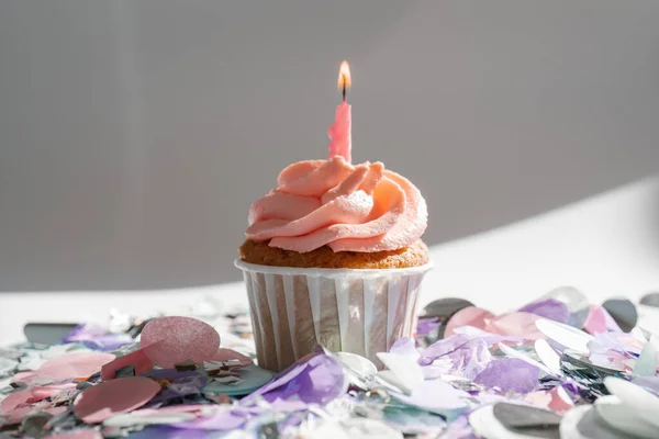 Un cupcake con una candela poggia su uno sfondo bianco con un'ombra. — Foto Stock