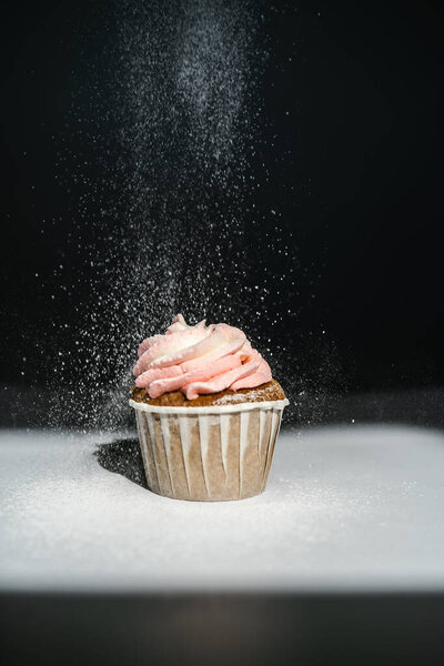 Cupcake on a dark background, which is sprinkled on top.