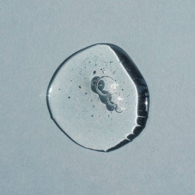 Gri arka planda bir damla şeffaf kozmetik jel.