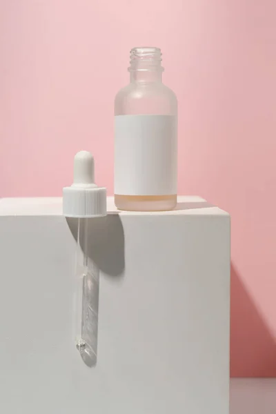 Cosmetic bottle with an eyedropper on a white-pink background.