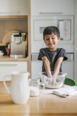 Çocuk mutfakta yemek pişirir. Unu temizler..