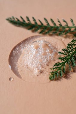 Bitkiler ve yapraklarla çevrili bej bir zemin üzerinde bir damla kozmetik jel..