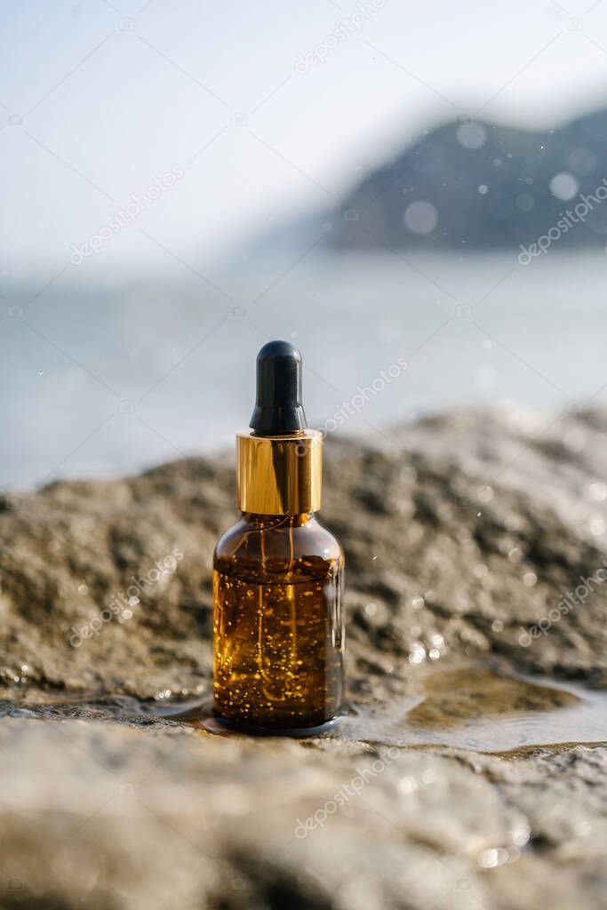 A bottle of serum on stones on a sea background.