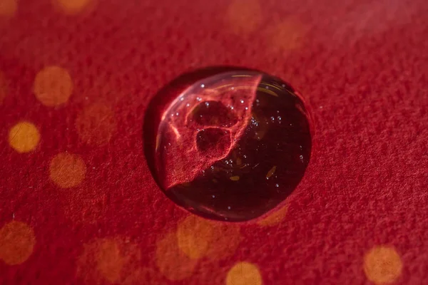 A drop of serum on a red background with bokeh.