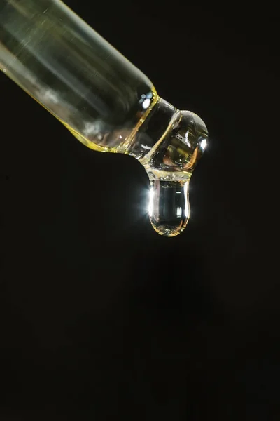 Pipeta cosmética com uma gota no fundo escuro. — Fotografia de Stock