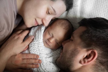Koyu saçlı beyaz bir çiftin güzel yeni doğmuş bebekleriyle yatakta yatıp onunla vakit geçirmesinin en güzel görüntüsü. Ailesinin arasında uyuyan tatlı bir çocuk.