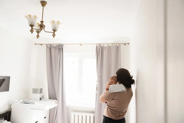 Benim güzel çocuğum. Kafkasyalı esmer kadının, yeni doğmuş bebeğini elinde tutarken pencerede duran esmer kadının arkası. Annelik ve mutlu çocukluk kavramı