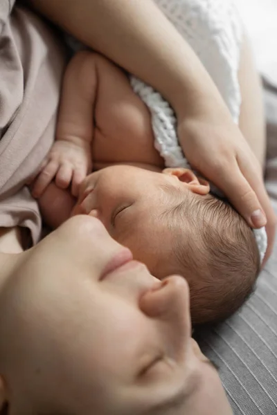 Tatlı annemizin sevgisi. Genç anne yeni doğmuş bebeğiyle eğlenirken, yatakta uzanıp onu kucaklıyor. Mutlu çocukluk kavramı 