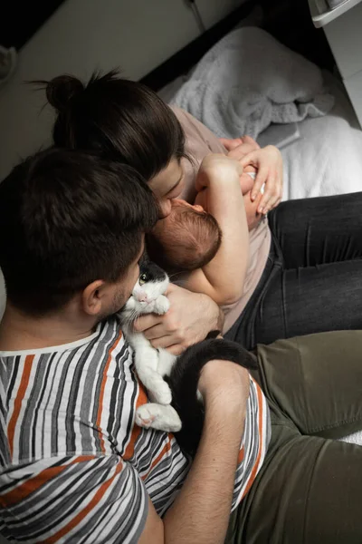 Yeni doğan çocuğuyla mutlu bir aile ilişkisinin yatağında otururken yüksek açılı görüntüsü. Adamın elinde oturan sevimli siyah beyaz bir kedi gibi. Stok fotoğrafı