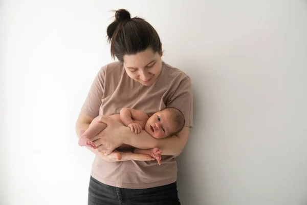 Genç anne yeni doğmuş bebeğiyle eğleniyor. Dikkatli ol, sevimli anne mutlu çocuğunu elinde tutuyor ve ona zevkle bakıyor.