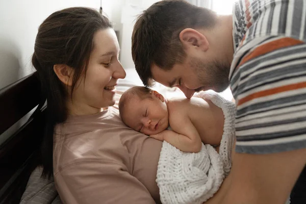 Baba, anne ve çocuğun yatakta uzanan ve çok mutlu hisseden güzel ailesinin yan görüntüsü. Baba burnuyla bebeğinin sırtına dokunuyor. Stok fotoğrafı