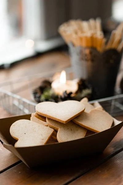 El işi kağıt kutusunda duran kalp şekilli kurabiyelerin dikey görüntüsü mum kenarındaki pencere eşiğinde duruyor. Arka planda kış manzarası. Tatlı kurabiye konsepti. Stok fotoğrafı