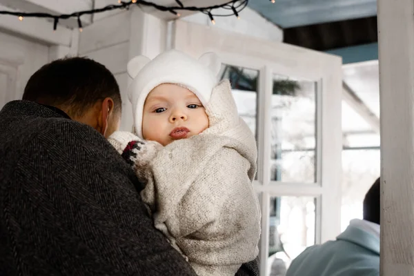 Anne ve babaların yeni doğan çocuklarıyla eve girişlerinin arkası. Babasının ellerinde otururken kameraya bakan tatlı bir oğlan çocuğu. Stok fotoğrafı