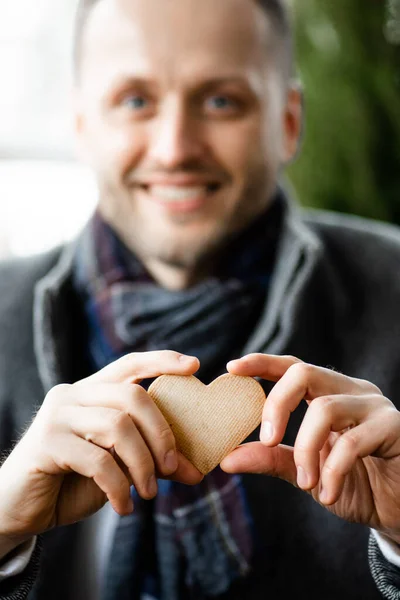 Elinde kalp şeklinde bisküviyle kameraya gülümseyen ve kameraya gösteren neşeli, tıraşsız adamın portre görüntüsü. Bir adamın ellerine odaklan.