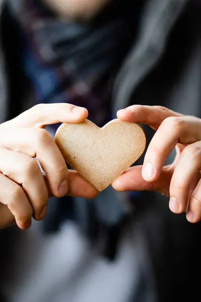 Bisküviyi kalp şeklinde tutan ve kameraya gösteren mutlu adamın yakın görüntüsü. Kurabiyeli bir adamın ellerine odaklan, adamın vücudu arka planda bulanıklaşır.
