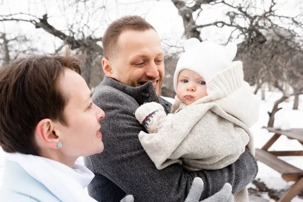 Mutlu ebeveynlik izinleri. Ebeveynler sevimli bebekleriyle eğlenirken, onu ellerinden tutup şefkatle gülümsüyorlar. Aile kış ormanlarında yürüyor.