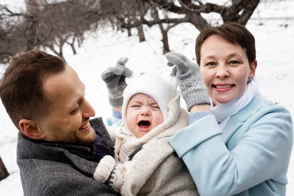 Ağlamayın. Sevimli beyaz kadın tatlı bebeğinin şapkasını düzeltirken kocası da onu ellerinden tutup birlikte vakit geçiriyordu. Kocası ağlayan bebeklerini sakinleştiriyor. Stok fotoğrafı