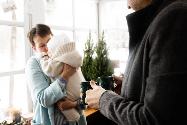 Birlikte ısınalım. Kısa saçlı, mutlu bir kadın onu kollarında tutarken tatlı bebeğine bakıyor. Kocası, karısı ve kendisi için çay getiriyor. Stok fotoğrafı