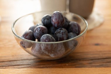 Ahşap bir arka planda cam bir kasede erikler. 