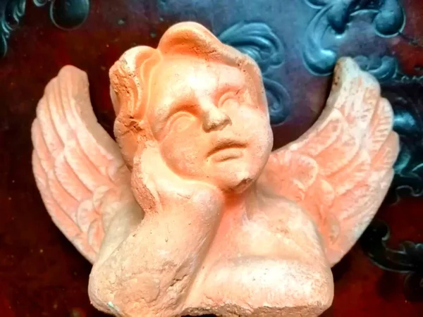戴着装饰品的守护天使可爱的梯形天使 以孩子的脸的形式躺在手掌上 后面是深红色的背景 是黑色的装饰品 — 图库照片