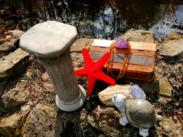 A mysterious treasure. On the stone shore of a small lake, there is a mysterious-looking treasure in a wooden box, surrounded by amethyst, citrines, small turtles and an ancient column.