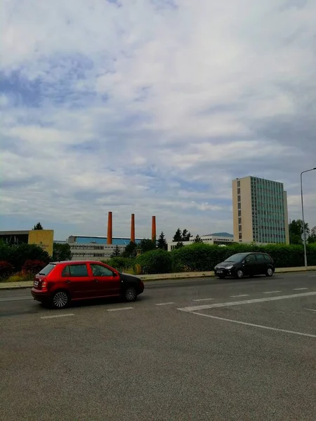 城市与一个工厂联合体 一个有汽车行驶的道路的城市 在它的后面是一个有三个高耸的砖制烟囱和一个地平线的大型工厂建筑群 — 图库照片