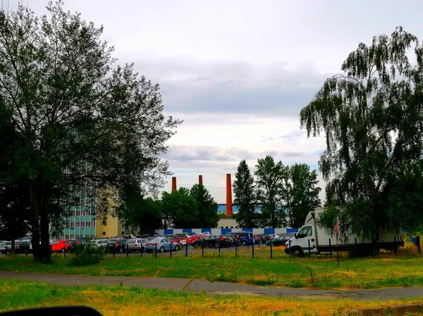 停在工厂前面 在一个满是汽车的城市停车场的视图中 可以看到前面有一条人行横道 后面是一个有三个高砖烟囱的工厂建筑群 — 图库照片
