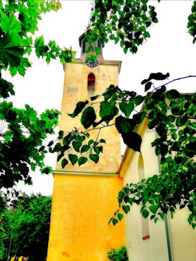 Sarı kilise kulesi. Ağaçların yeşil dalları antik kilisenin arka planında bir kule ve ağaçla kısmen örtüşüyor.. 