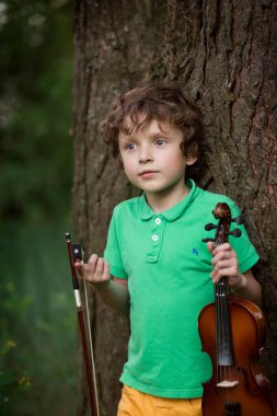 Kıvırcık saçlı yetenekli çocuk gün batımında doğada keman çalar.