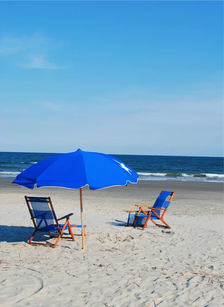 Bir çift mavi plaj sandalyesi ve şemsiye.
