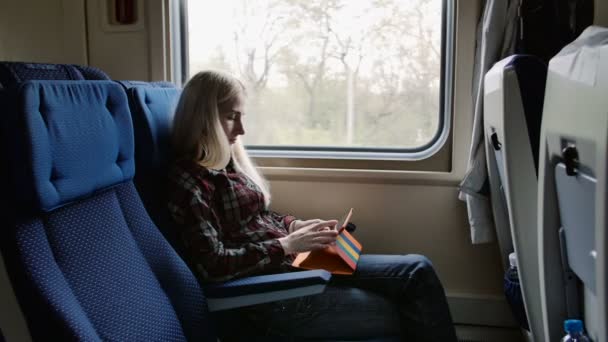 Jeune femme utilisant une tablette dans un cas coloré tout en voyageant en train — Video