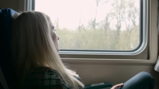 Mujer joven caucásica mira a través de la ventana mientras viaja en tren — Vídeo de stock