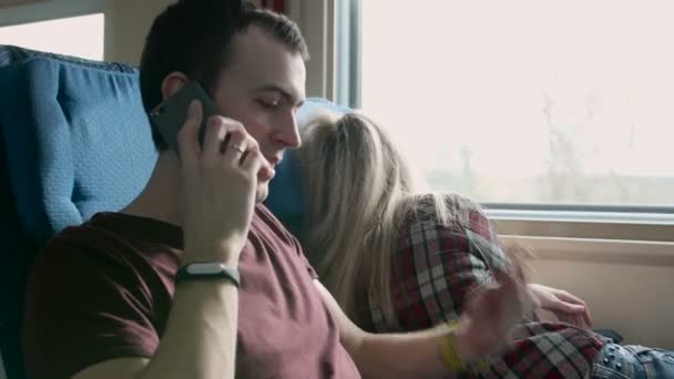 Rozhněvaný mladý muž s někým promluvit na telefonu do jedoucího vlaku. Smích žena na něj — Stock video